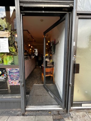 Glass door with black, metal frame ahead. Push from left to open.