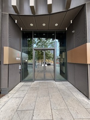 From sidewalk facing venue. Open archway ahead. Glass doors on back. Doors slide to open from center automatically.