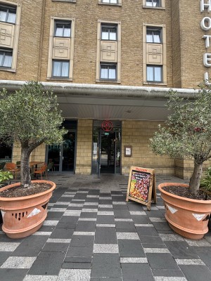 From sidewalk facing venue. Opening ahead between planters. Path down center to doors on back.