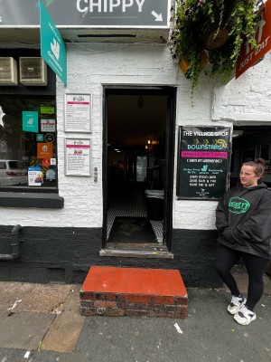 Two steps up to black, wooden door ahead. Push from left to open.