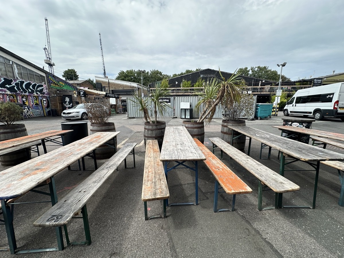 From end of picnic benches facing straight. Tables and benches ahead. Planters along back of seating.