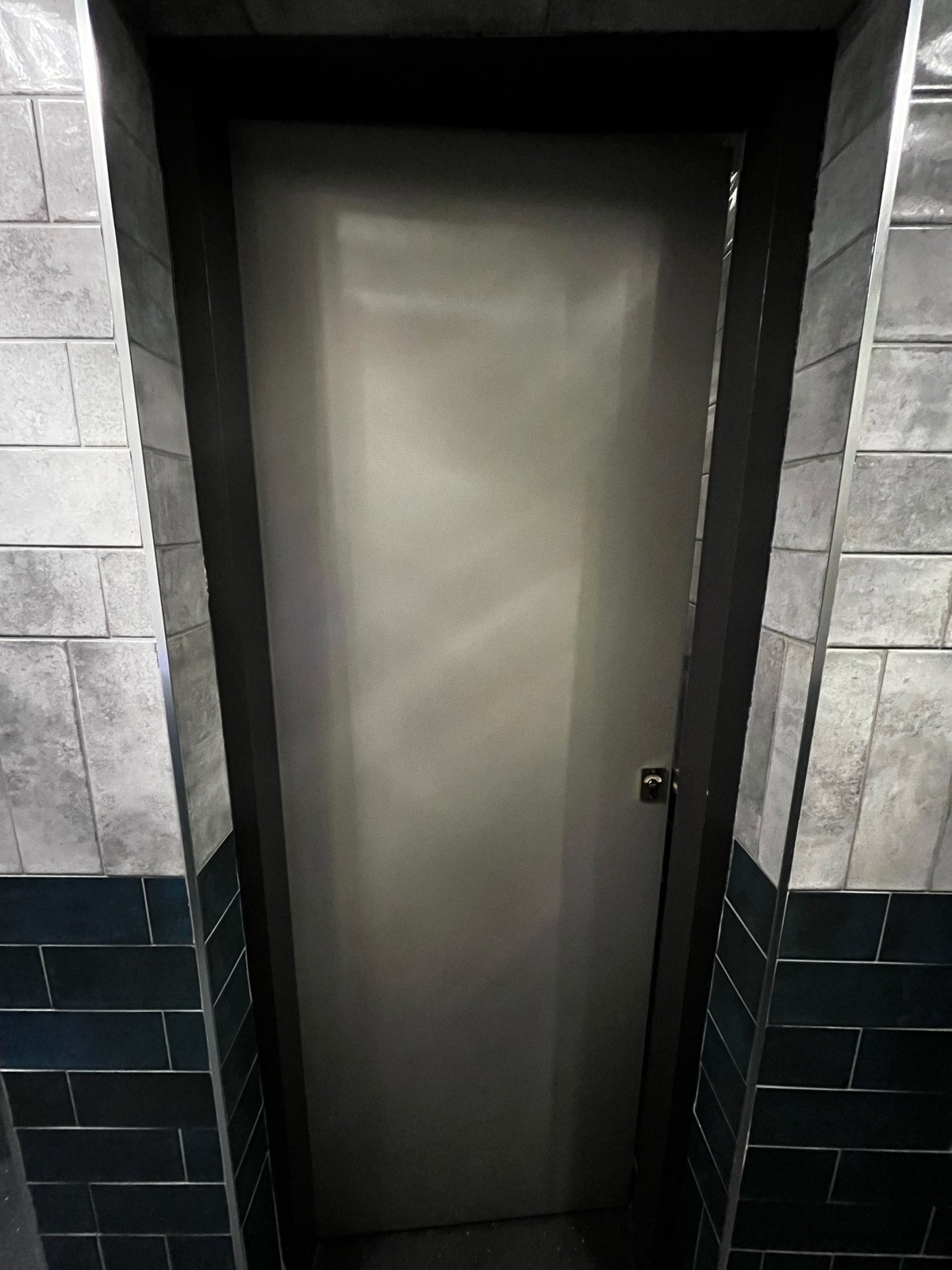 From preceding door, facing right, Grey wooden cubicle door ahead. Push from right to open.