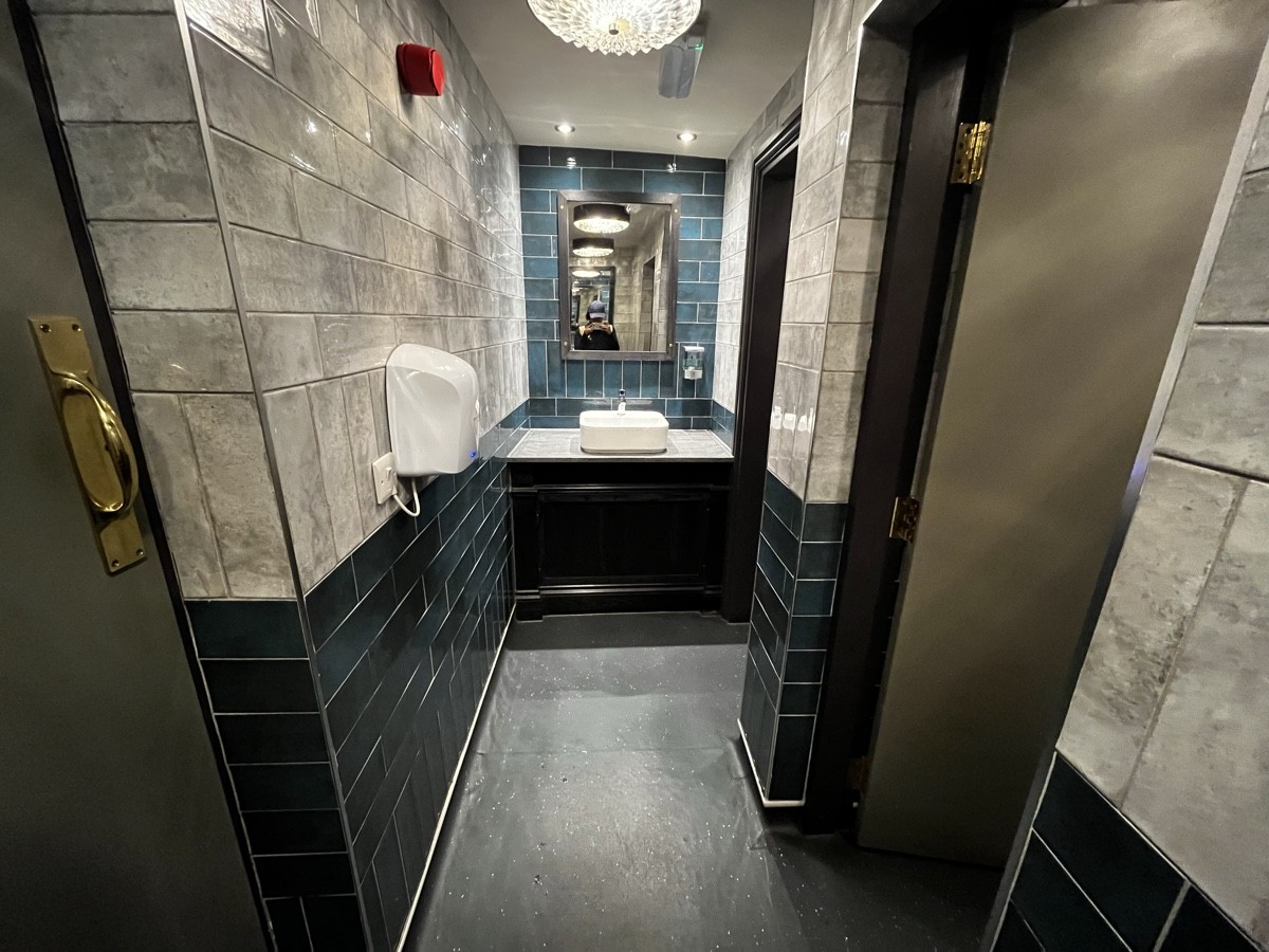 From preceding door facing left. Cubicles along right. Sink at end of path ahead.