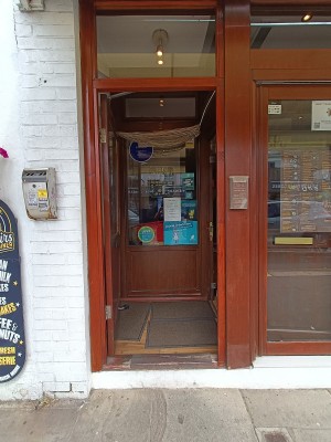 Glass door with brown, wooden frame. Push from right to open.