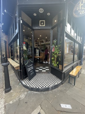 From street facing venue. Opening ahead. Step up at foot of opening. Glass door with black frame at back. Pull metal handle from right to open.