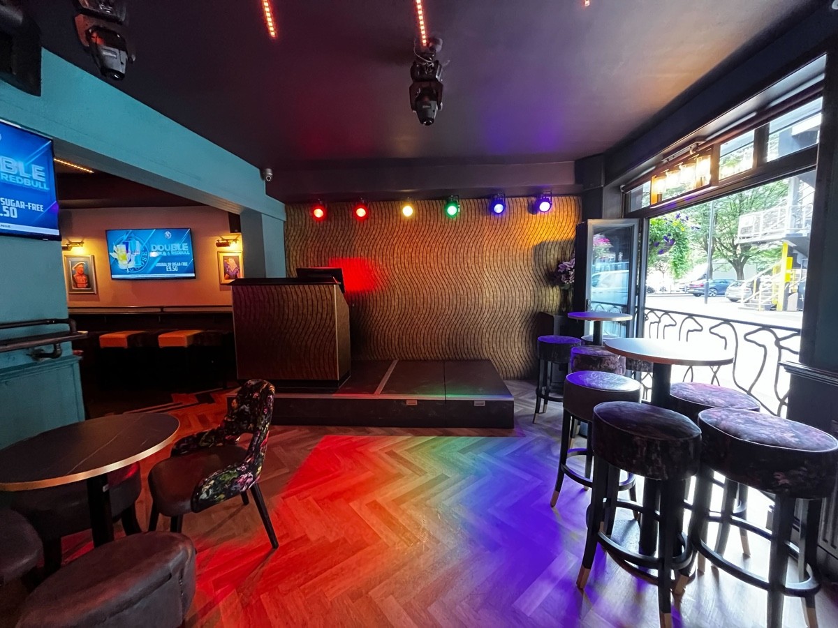 From entrance facing right. High teams and stools to right. Fence behind tables. Music stage to centre back. Tables and chairs to left.