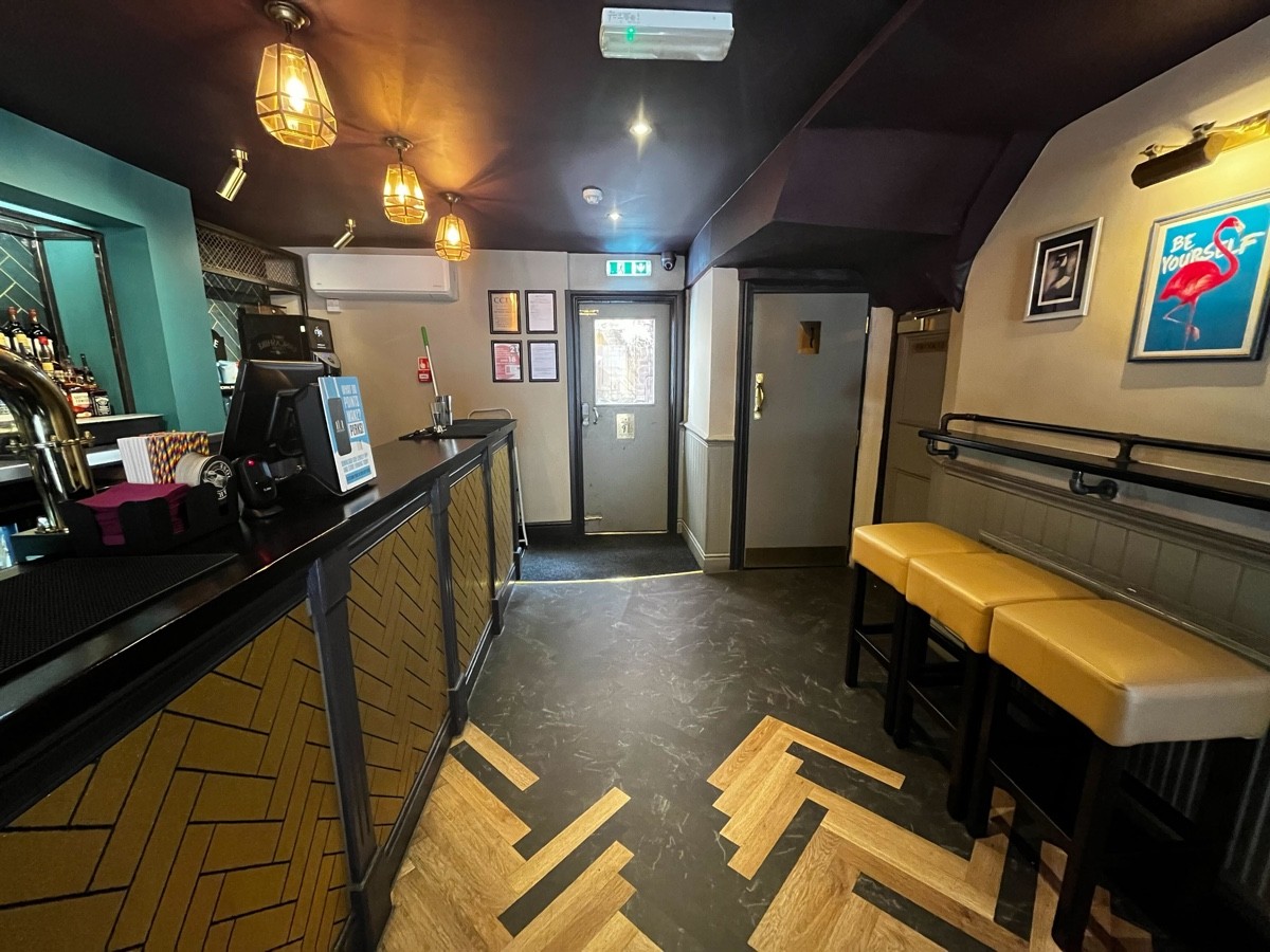 From left of column facing straight. End of bar area to back left. Cushioned stools and small high table to right.