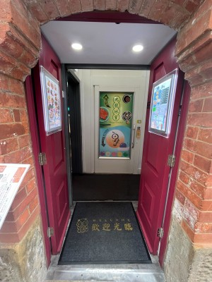 From sidewalk facing venue. Open archway ahead. Red doors behind. Push doors from centre to open.