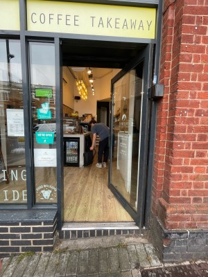 Facing glass door with black frame. Push on left to open.