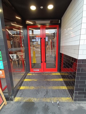 Opening ahead. Built-in ramp up to glass doors with red frame ahead. Pull black, metal handles in middle to open.