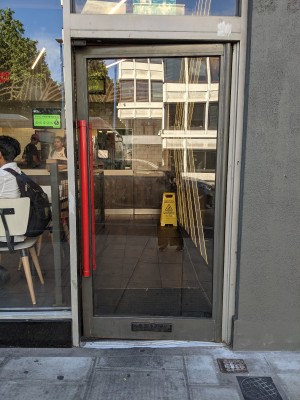 Glass door with metal frame and red handle. Push from left to open.