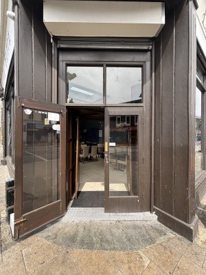 From sidewalk facing venue. Glass doors with wooden frame ahead. Pull from handles in center to open.