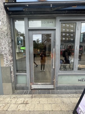 Glass door with grey frame ahead. Push silver metal handle from right to open.