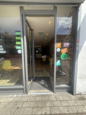 Glass door with grey frame ahead. Push grey handle from right to open.