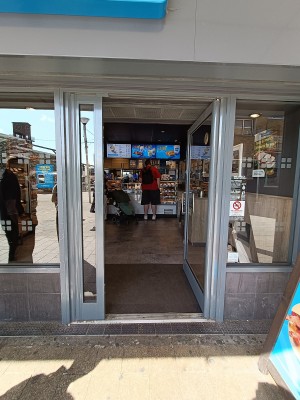 Glass door with grey, metal frame. Push silver handle on left to open.