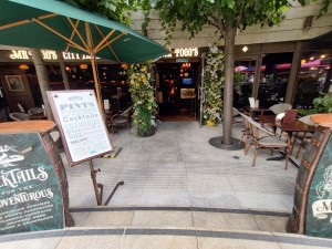 From street, facing venue. Steps ahead. Tables and chairs on both sides. Path in between. Doors at back