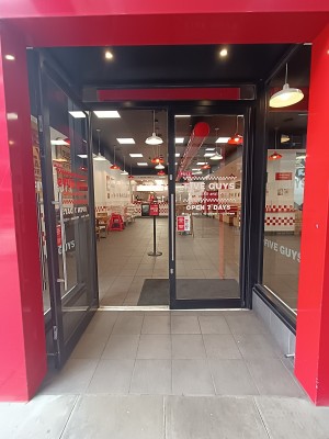 From street, facing venue. Opening ahead to glass doors with black, metal frame. Pull silver handles from middle to open.