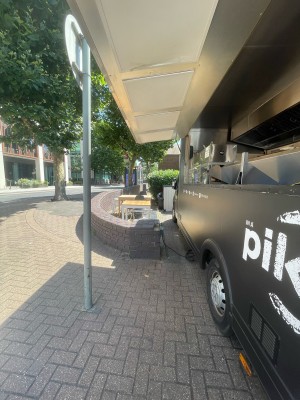 From street facing venue. Opening ahead. Counter within truck along right. Grey pillar on left. Seating beyond it.