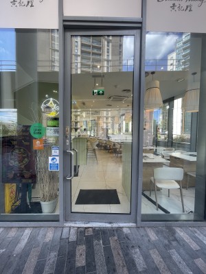 Glass door with grey frame ahead. Push silver metal handle from left to open.