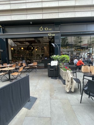 From street, facing venue. Restaurant barrier on left. Tables and chairs to its left. Welcome desk on back right.