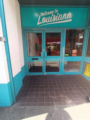 Glass doors with blue, metal frame ahead. Pull handles from middle to open.