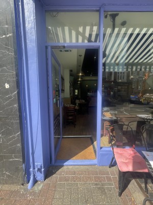 Glass door with blue frame ahead. Push blue metal handle from right to open.