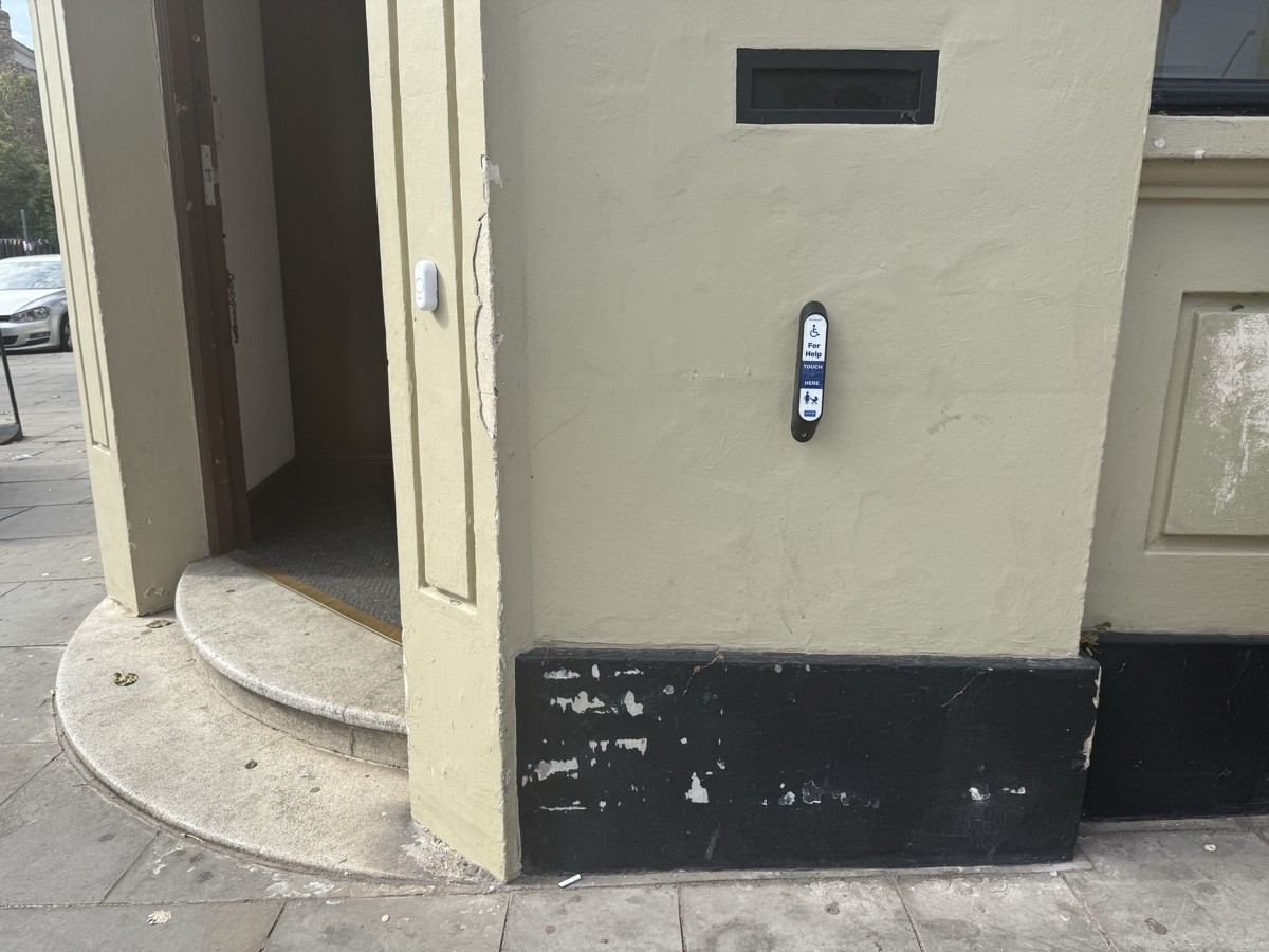 Right of the entrance, a touch-based assistance bell is placed near the café bell for wheelchair users or those with buggies needing help to enter.