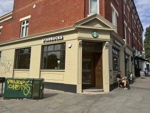 L-shaped corner cafe with 2 semi-circular steps at entrance and a heavy push door; limited space for a wheelchair user to access or enter easily.