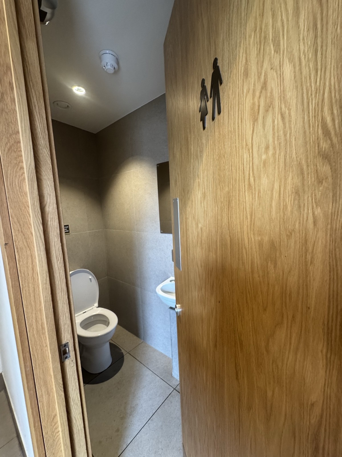 The toilet offers minimal space with a small standing-height sink, just enough for basic use.
