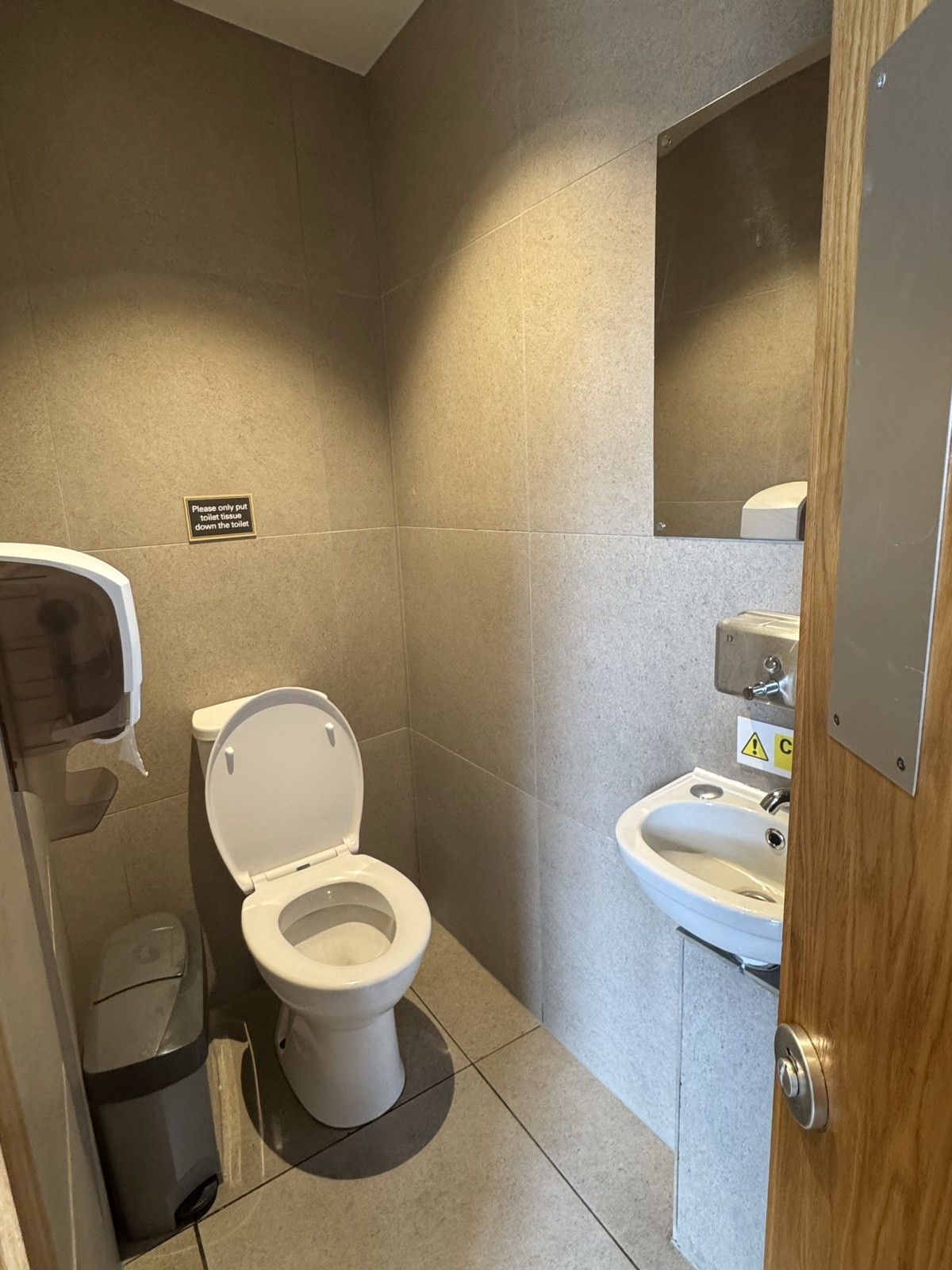 The toilet has limited space, a small standing-height sink, and a touch-free sanitary bin for convenience.