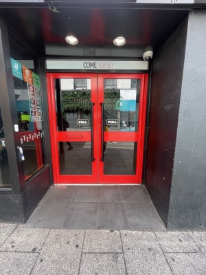 Glass doors with red frame ahead. Pull black metal handles from centre to open.