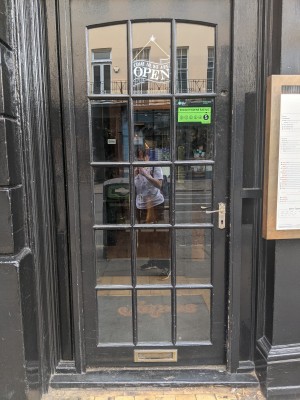 Glass door with black frame and gold handle. Push from right to open.