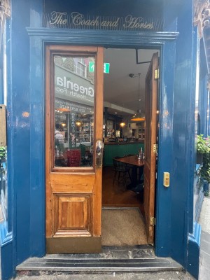Glass paneled doors with wooden frame. Push in center to open. Doorbell for assistance on right.