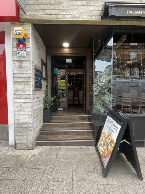From street facing venue. Opening ahead with four steps up. A-frame sign to right.