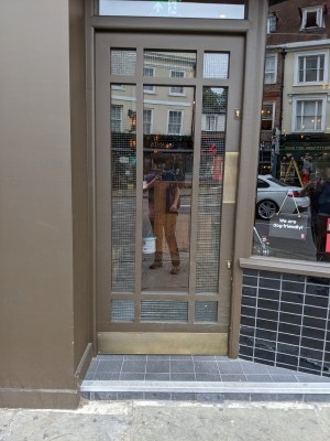 Glass door with brown frame and gold handle. Push from right to open.