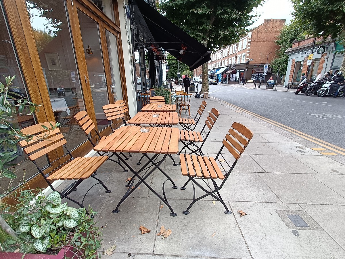 From after planters, facing straight. Tables and chairs ahead along left.