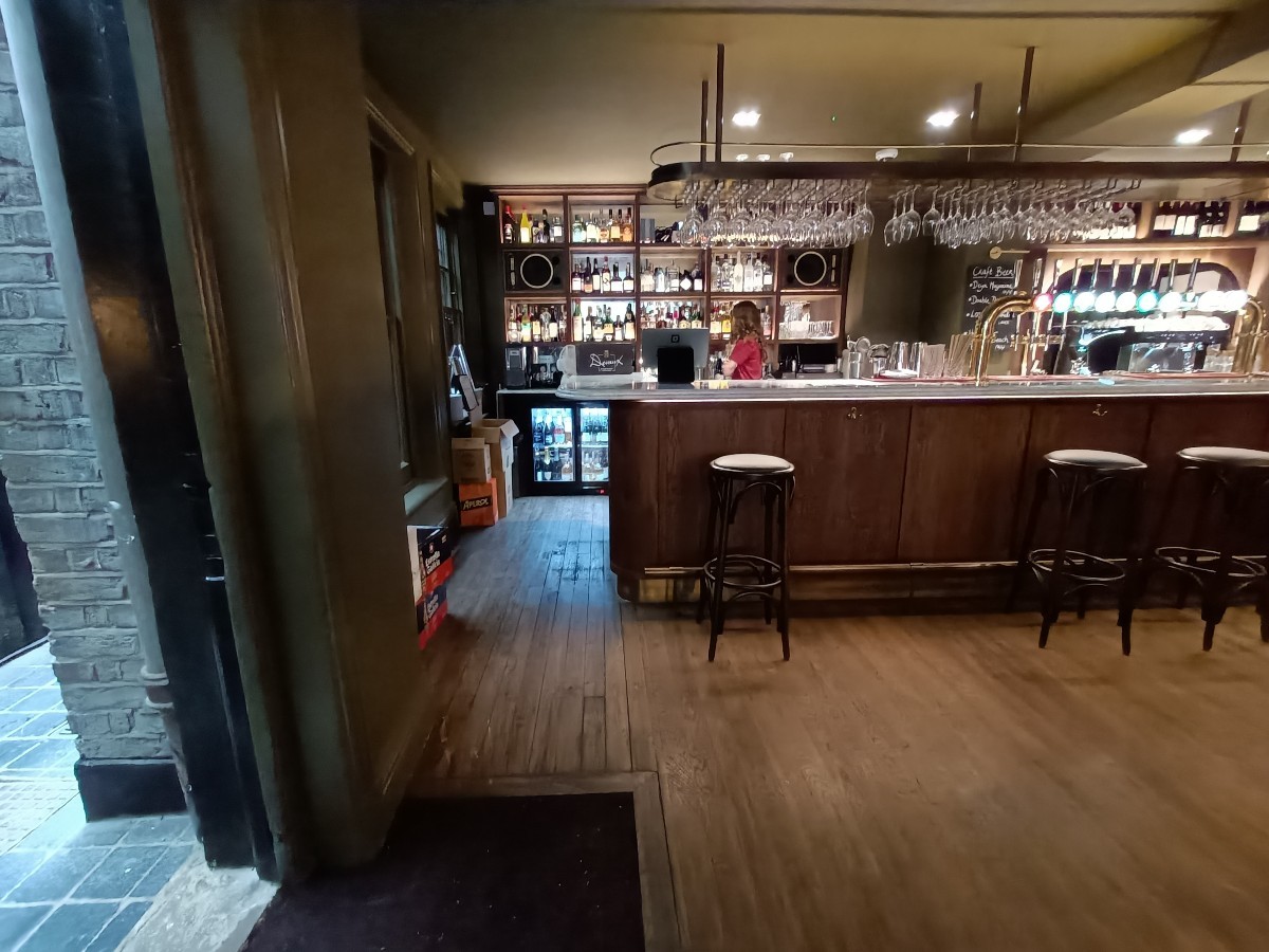 From after half-booths and stools, facing straight. Doorway to bathroom on left. Bar counter and stools along back right.