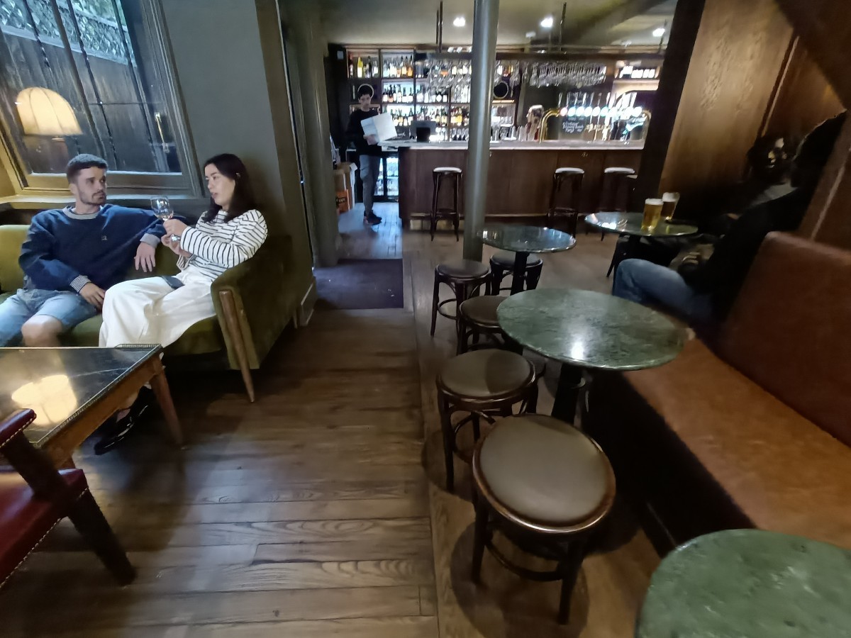From end of half-booths and chairs, facing straight. Couches and low table on left. Half-booths and stools along right. Pillar behind.