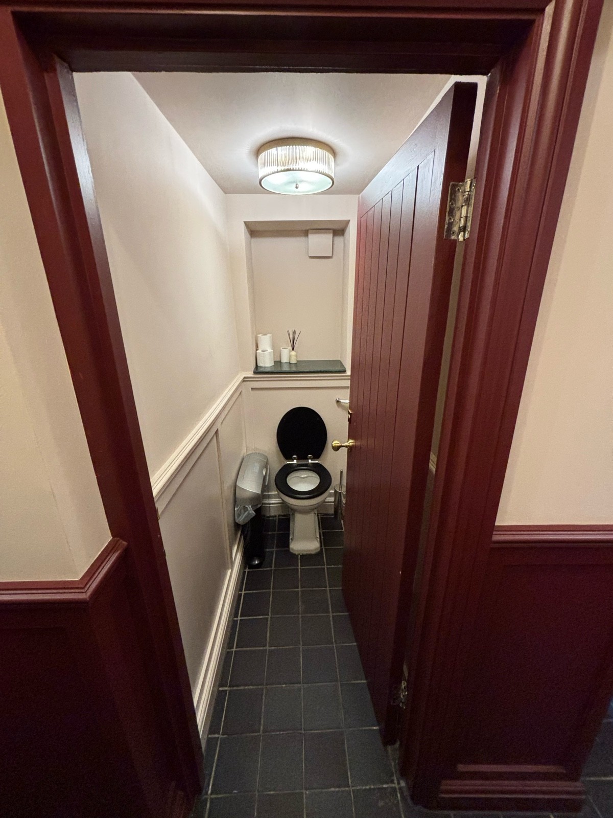 From from opening facing right. Dark red door ahead. Push from left to open. Toilet on back wall.