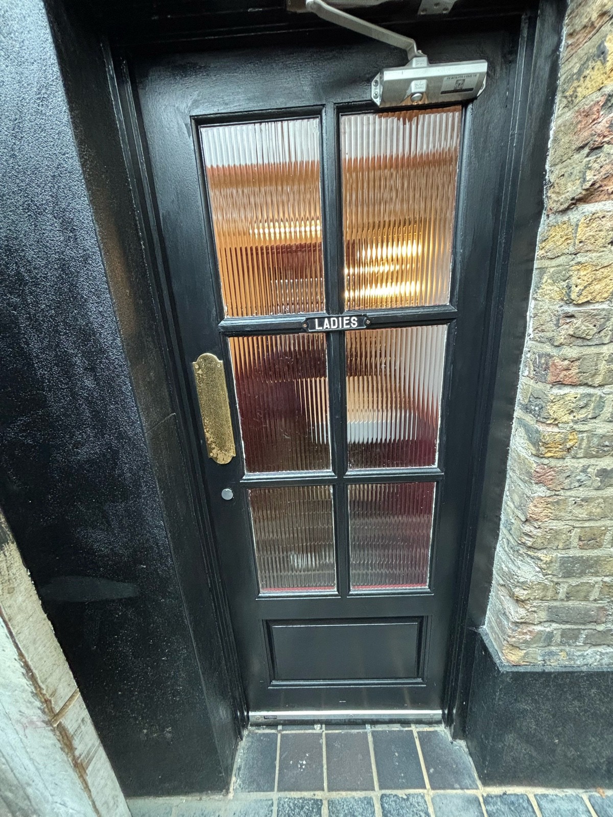 From end of corridor facing right. Dark green wooden door with glass panels ahead. Push door to open via brass pad.