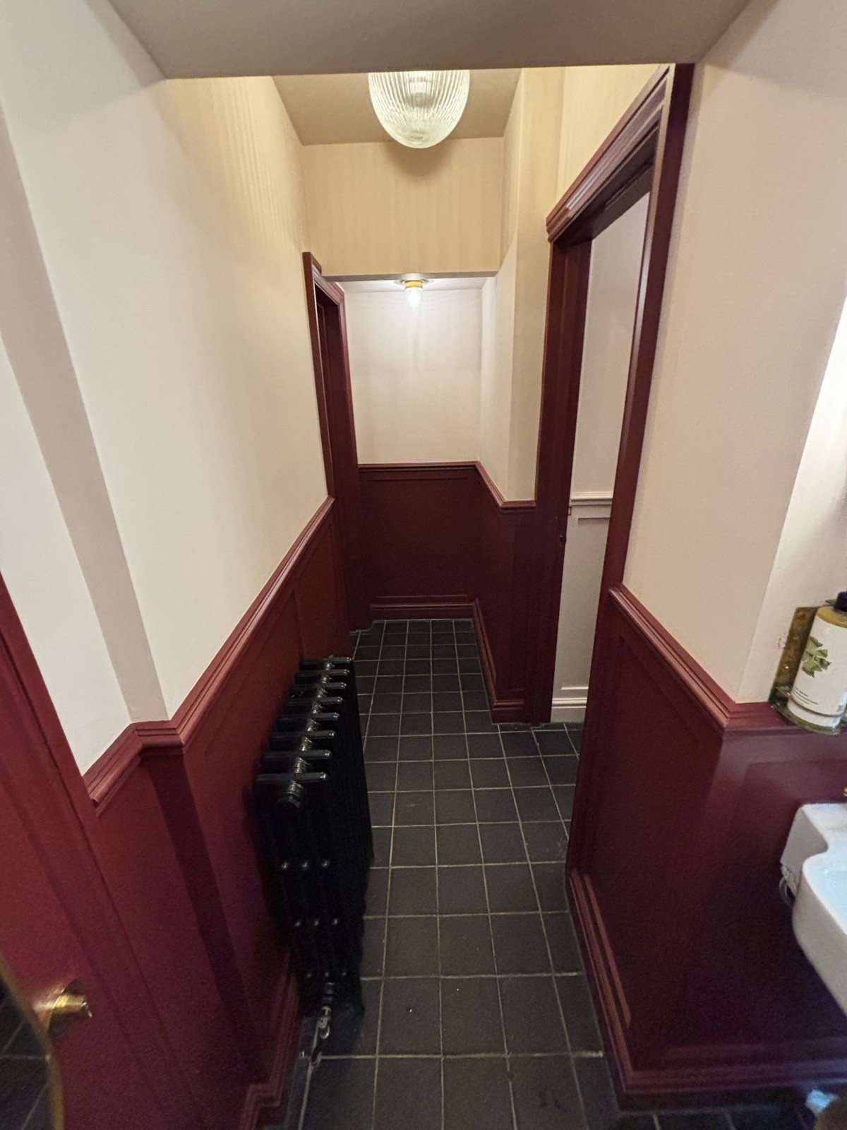 From end of sinks facing right. Open archway ahead. Path behind with cubicles on right and back left. Radiator on left.
