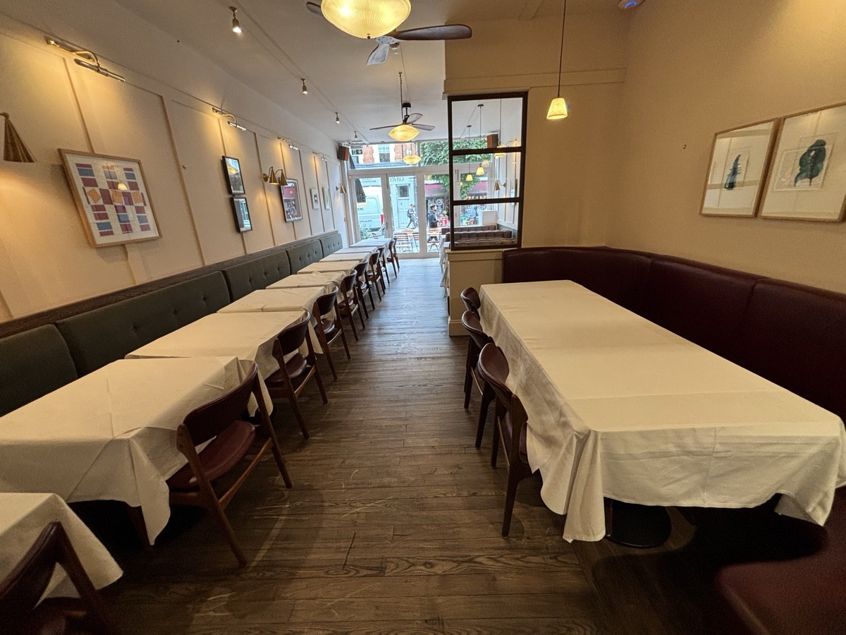 From opening facing straight. Half booth with tables and chairs on both sides. Glass divider on back right.