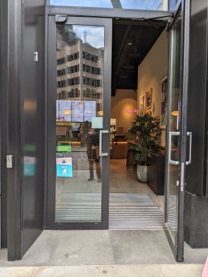Glass doors with grey frame and silver handles in centre. Pull to open. Doorbell left of doors.