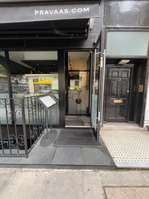 From sidewalk facing venue. Glass door with black frame on back. Pull door via metal handle on left to open.