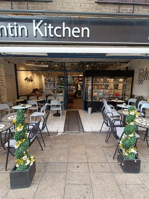 From street, facing venue. Planters on both sides. Outdoor seating behind. Path in middle to doorway.