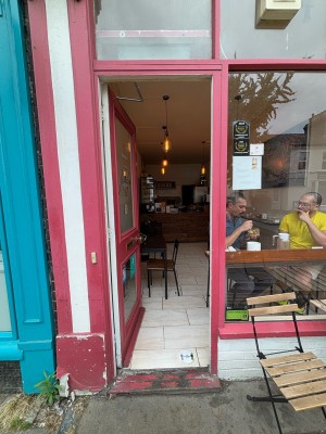 Glass doors with red frame ahead. Push from right to open. Doorbell for assistance on left of door.