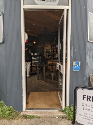 Glass door with white frame. Push from white handle on left to open. Doorbell right of door.