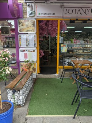 From sidewalk facing venue. Bench along left. Tables and chairs along right.