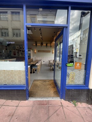 Glass door with blue frame ahead. Push metal handle from left to open.