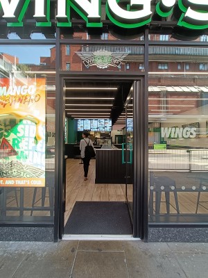 Glass door with black, metal frame. Push green handle on left to open.